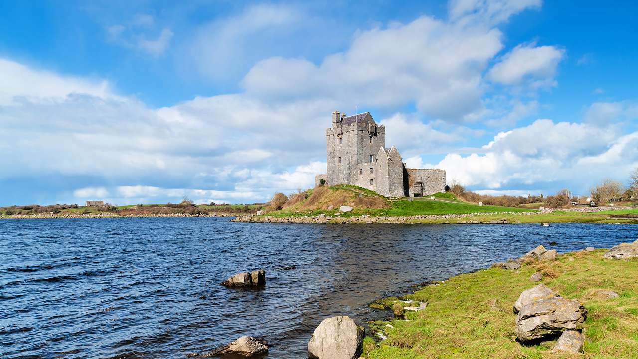 A stone castle by a body of water near grassy coasts and small rocks