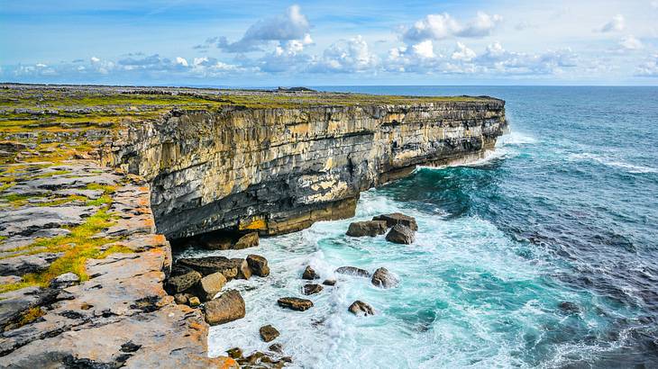 A high-angle view of a cliff near the ocean under a blue sky with clouds