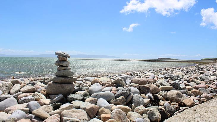 A pile of stones by the coast of a rocky beach under a blue sky