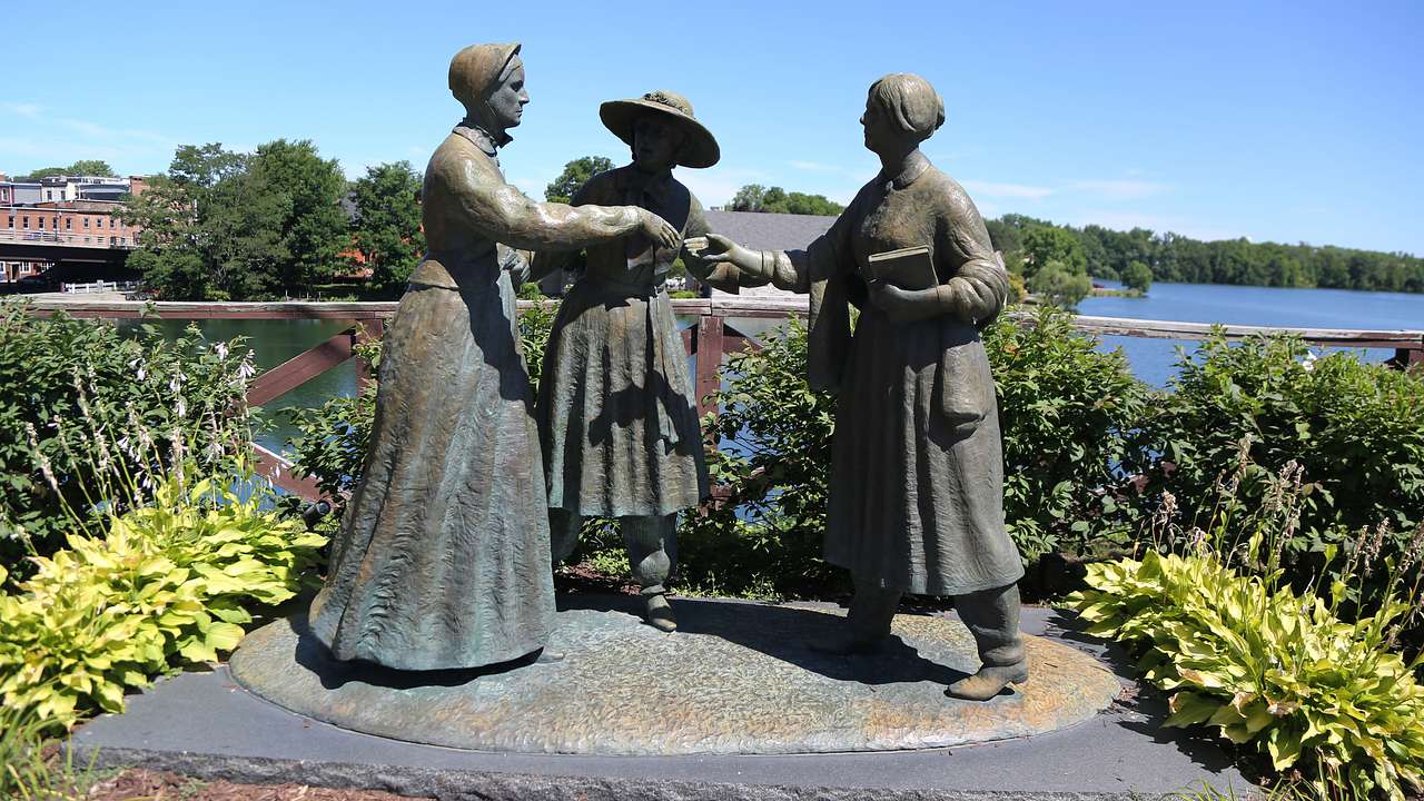 Statues of three women surrounded by greenery and a body of water