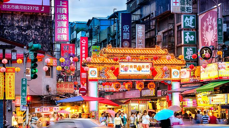 People in front of the Raohe Street Night Market sign as cars pass