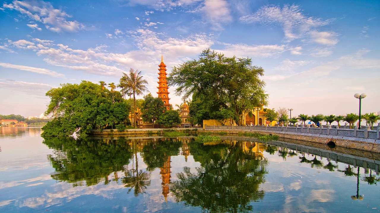 A lake surrounded by trees, a red-orange pagoda, and a partly cloudy sky