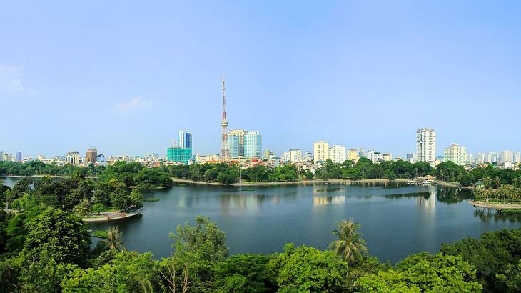 A lake surrounded by green trees with a city skyline on one side under a blue sky