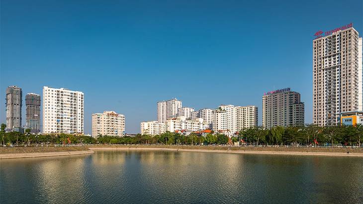 A lake next to green trees and city buildings