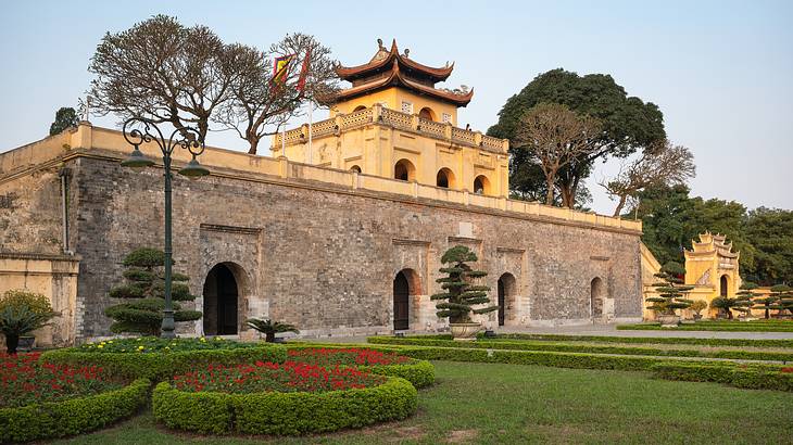 An Asian temple-style building with grass and bushes in front and trees behind it