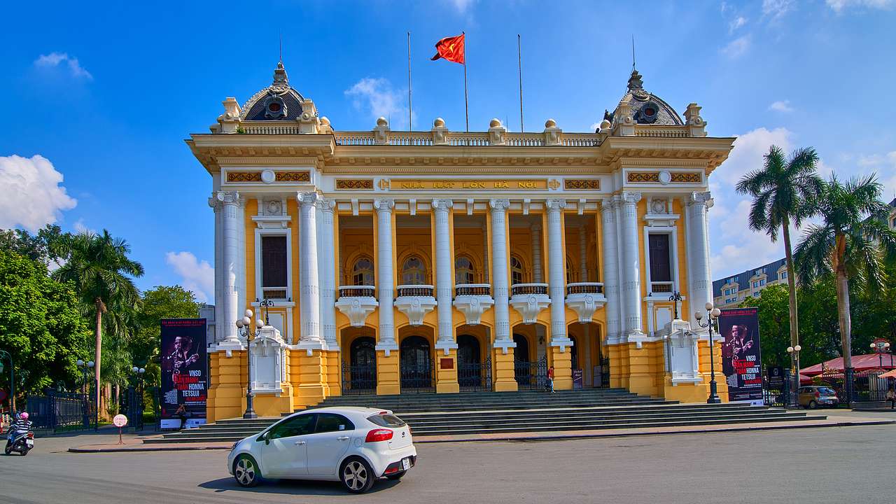 A yellow and white building with a flag on top and a road with a car in front