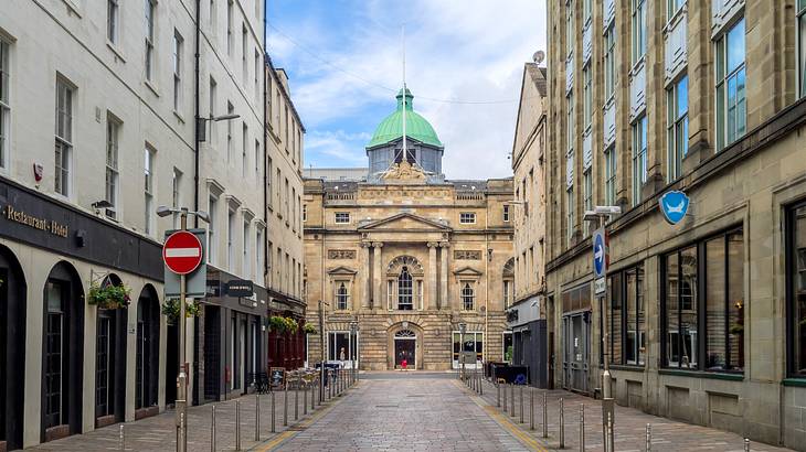 An empty alley surrounded by buildings leading to a stone building with a dome