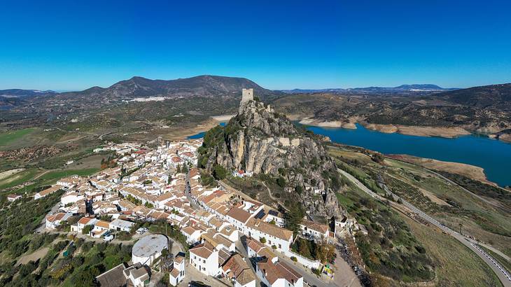 An aerial shot of a village near the foot of a rocky mountain and a body of water