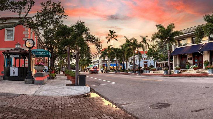 A street with colorful shops, restaurants, & palm trees on each side under a red sky