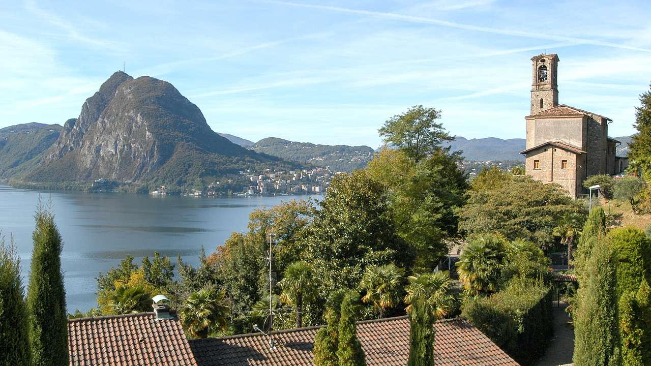 A body of water next to trees and a building, with a mountain in the background