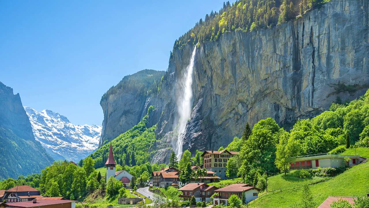 A tall waterfall flowing down a cliff next to greenery and small houses