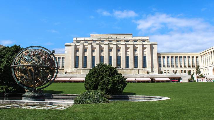 A large stone building with columns next to the grass, a bush, and a globe statue