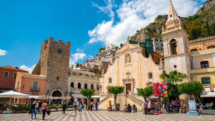 Tourists in an old town square with historical buildings and small trees around it