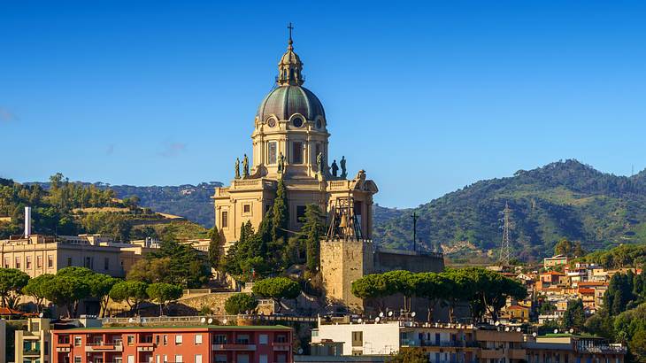 A temple building with a dome and a cross on top of it next to a green mountain