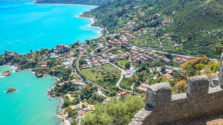 Ruins of a castle wall overlooking a historical town and a bay with blue water