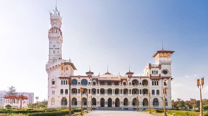 Montaza Palace's grand exterior surrounded by a pathway, lamp posts, and green grass