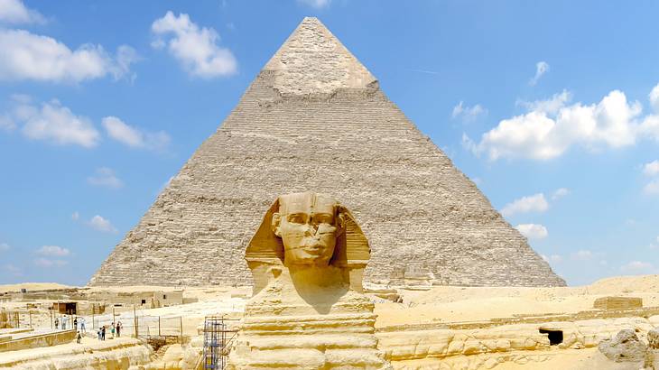 Statue of a sphinx with a large pyramid behind it situated in a desert