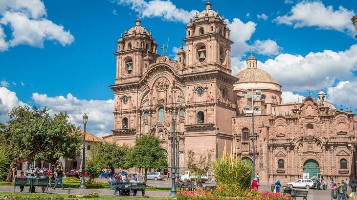 People in a park near an old intricately-designed church with two bell towers