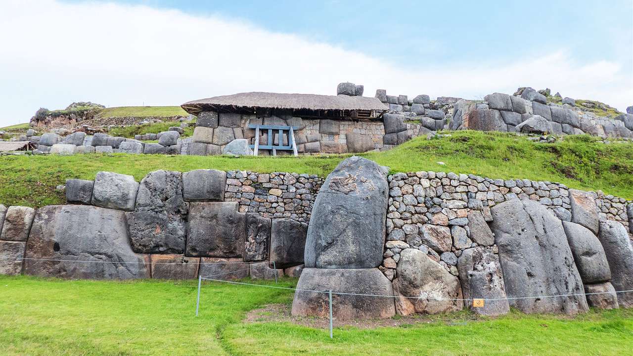 Ancient stone ruins arranged like short walls around a hut in a hilly terrain