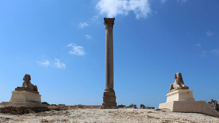 A pillar standing in the middle of two sphinx against a blue sky