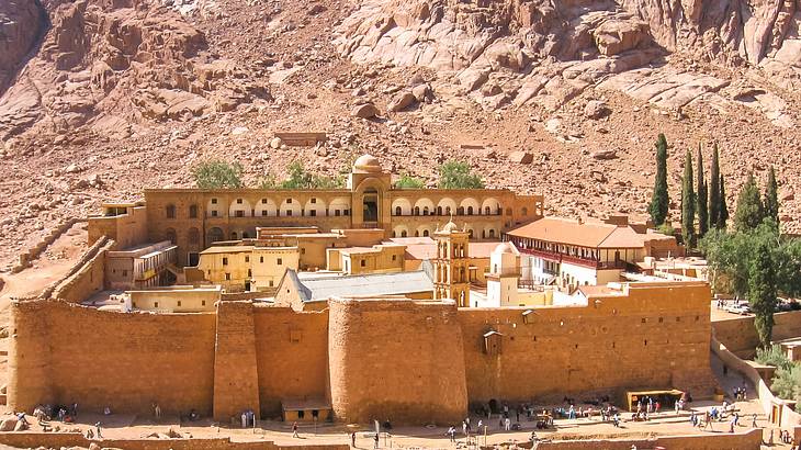 Aerial view of a walled monastery below a mountain with people outside Aerial view of a walled monastery below a mountain with people outside