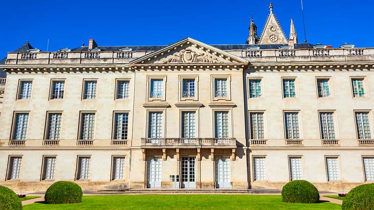 A facade of an old building with many windows near a lush garden