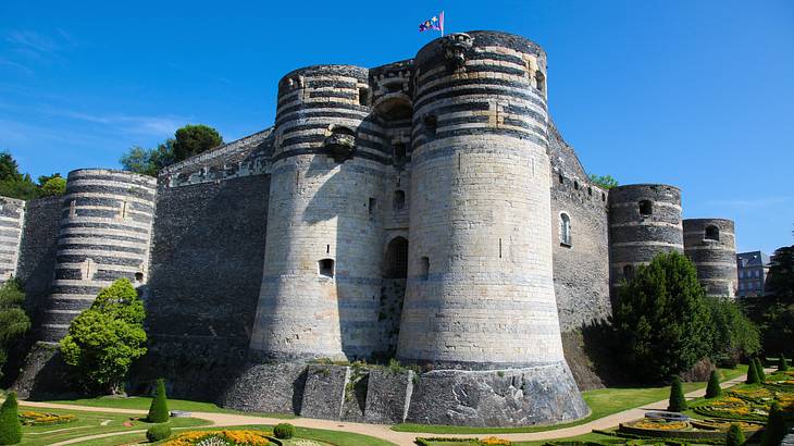 A low-angle shot of a stone castle near a landscaped garden