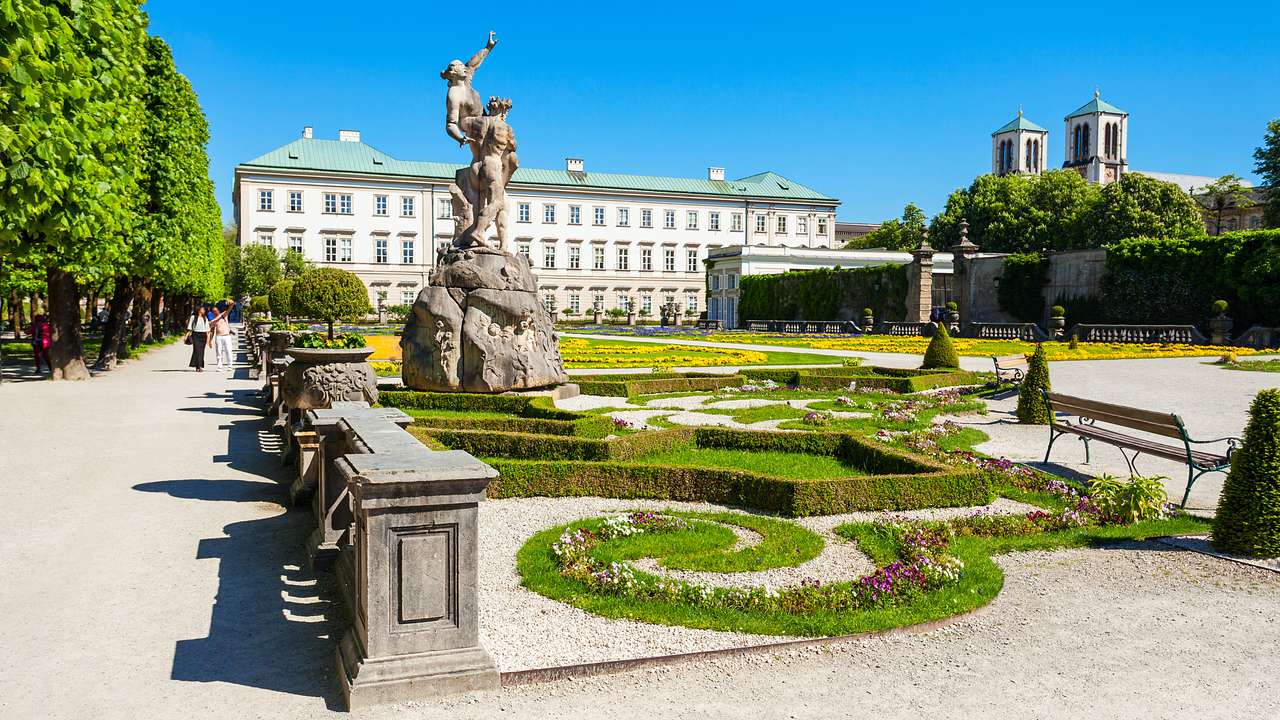 A landscaped garden with statues and trees near a large building