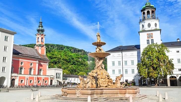 A water fountain with sculptures near buildings with spires