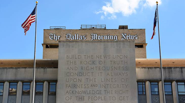 A facade of a building with waving flags and a sign saying "The Dallas Morning News"