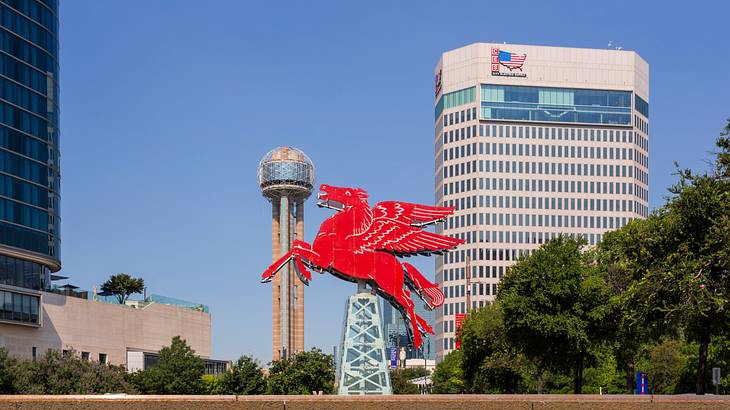 A hanging structure of a red pegasus surrounded by buildings and trees
