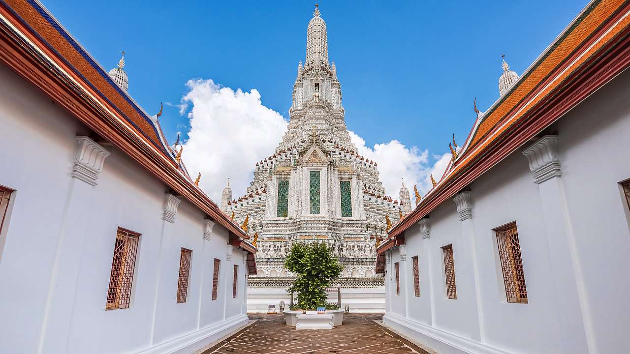 An intricately designed white temple from below facing two low buildings