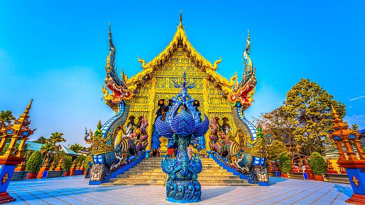 A blue statue with detailed carvings in front of a yellow temple with stairs