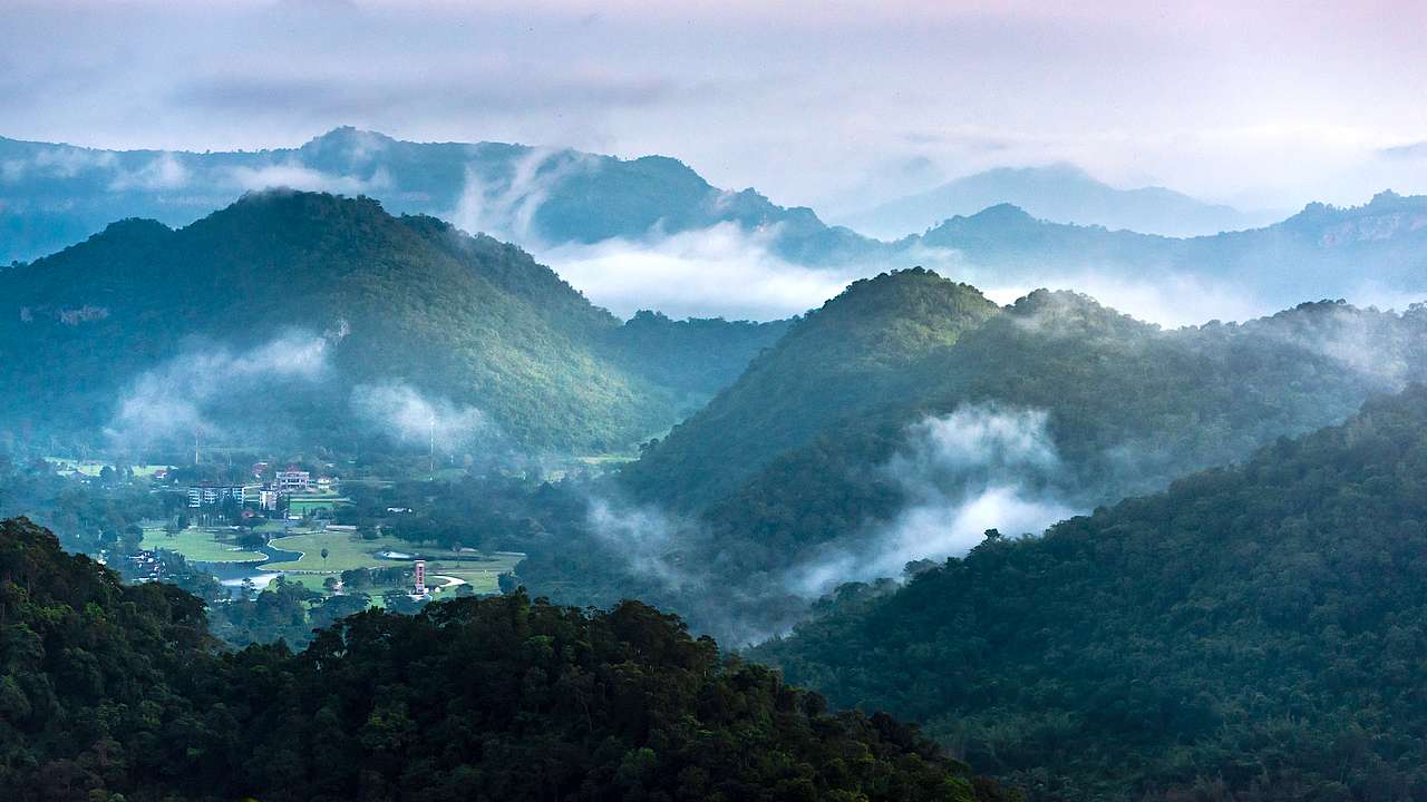Tree-filled mountain tops with foggy areas and a village in the center from above
