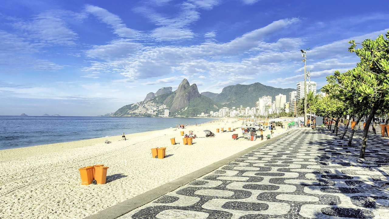 People on the beach near a mosaic walkway with a mountain in the background