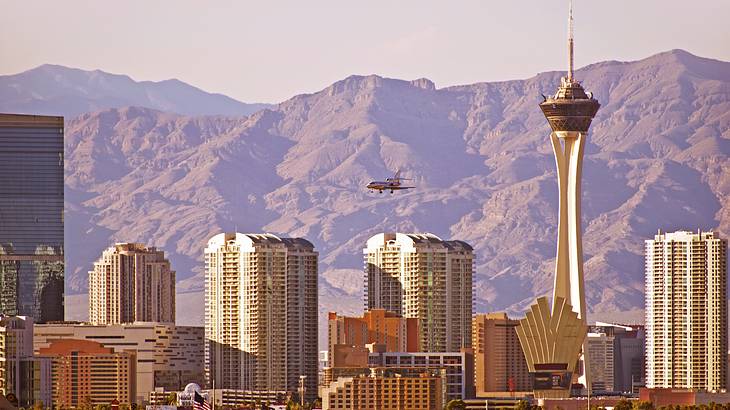 A city skyline with a rocky mountain in the background and a plane landing