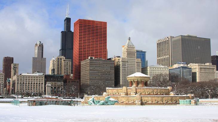 A city skyline next to a park covered with snow under a cloudy sky