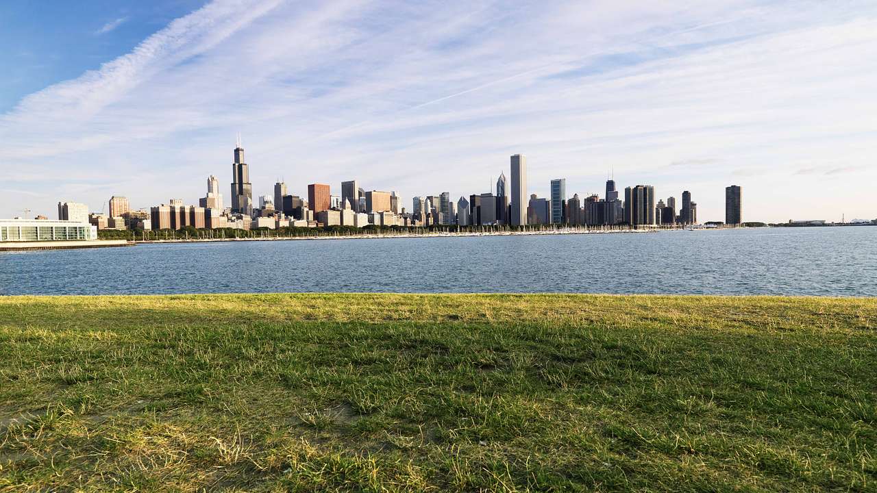 A body of water next to a park and a city skyline under a partly cloudy sky