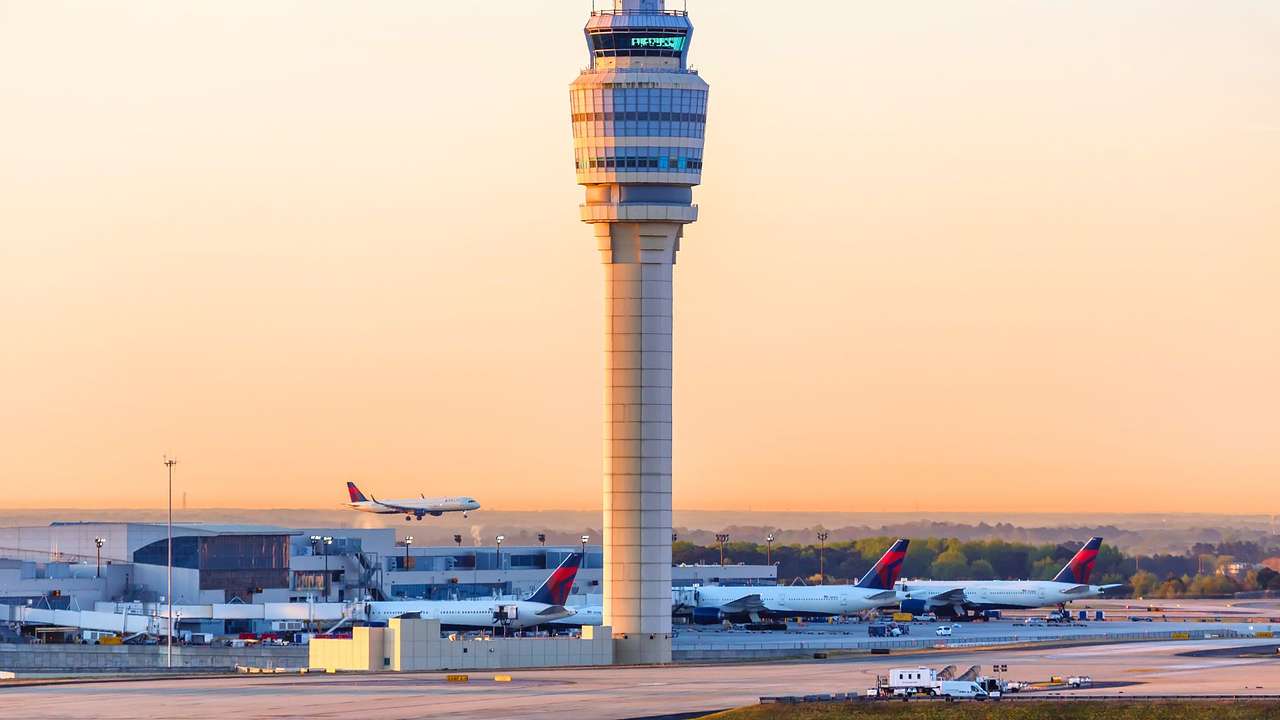 An air traffic control tower surrounded by airplanes at sunset