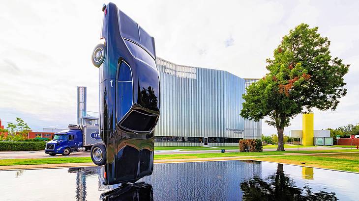 Shallow water with a car in the middle tilted vertically near a tree and a building