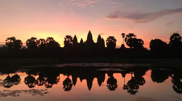  Schwarze Tempel- und Baumsilhouetten, die sich bei Sonnenaufgang im Wasser spiegeln