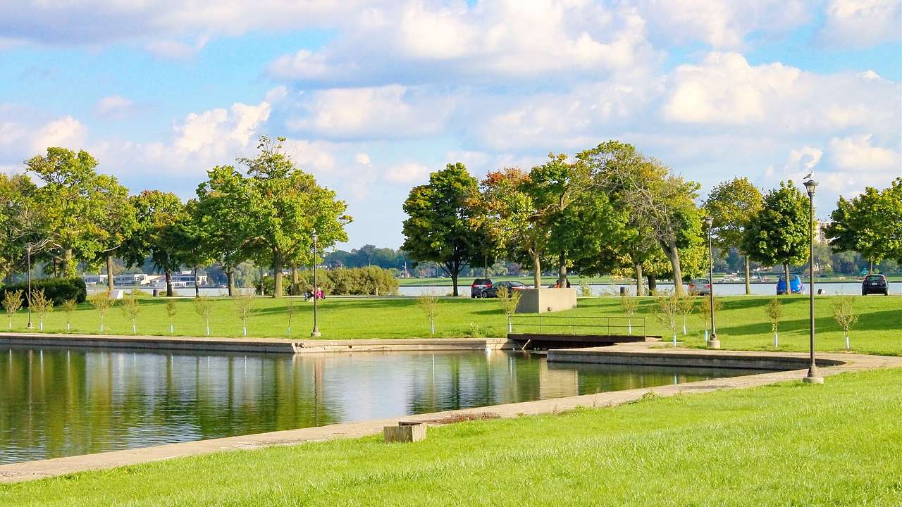 A park with a lawn, trees, and an artificial lake under a cloudy sky