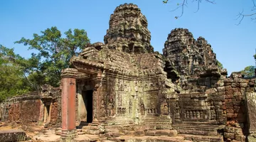 O exterior de um antigo templo contra um céu azul com o verde das árvores atrás