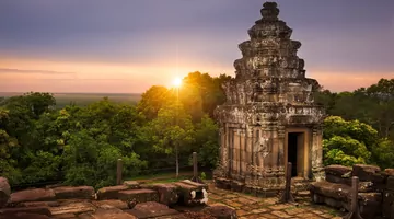 Il sole che tramonta dietro alberi verdi e un vecchio tempio 