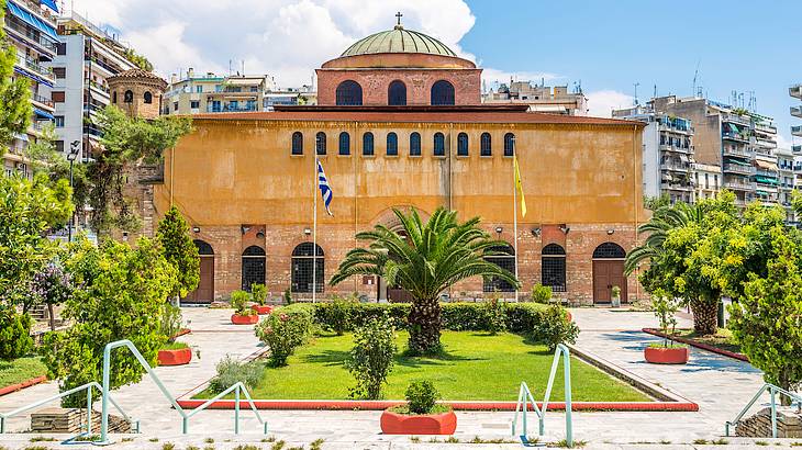 A domed reddish Byzantine church, in Thessaloniki, Greece facing a garden and stairs