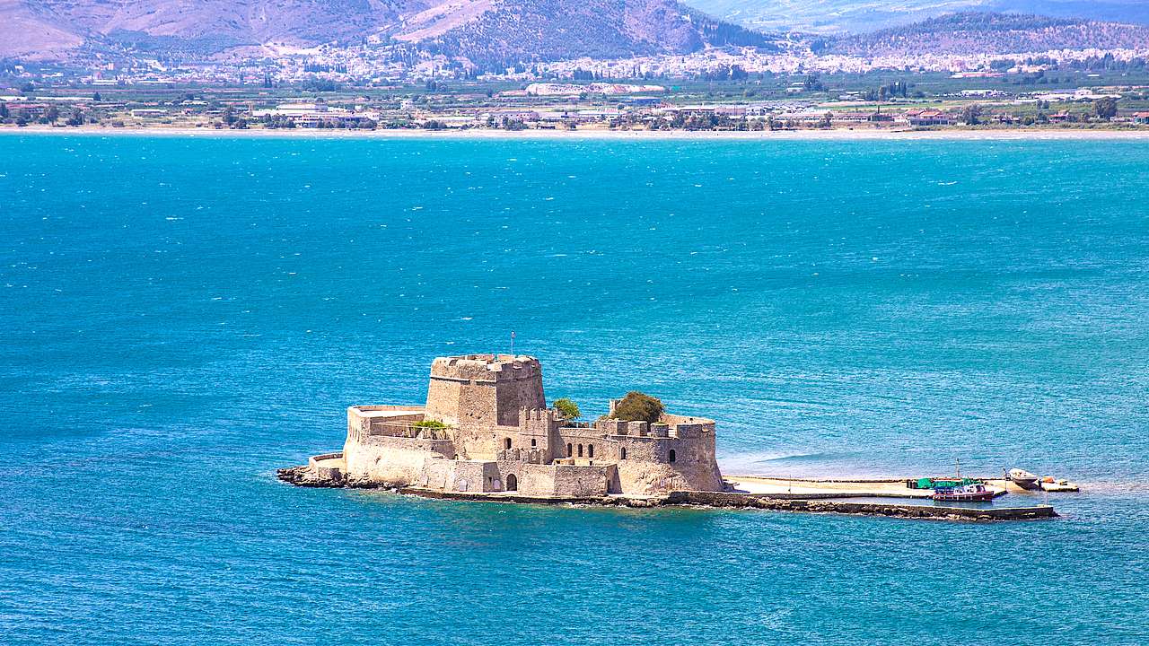 A castle fortress surrounded by water and mountains in the back, in Nafplio, Greece