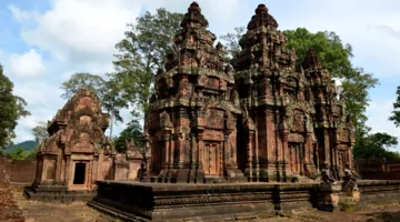  Kleine rötliche Tempel nebeneinander gegen einen teilweise bewölkten Himmel