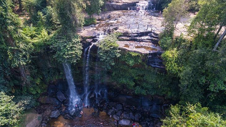An aerial shot of a small waterfall cascading over a cliff amongst trees An aerial shot of a small waterfall cascading over a cliff amongst trees