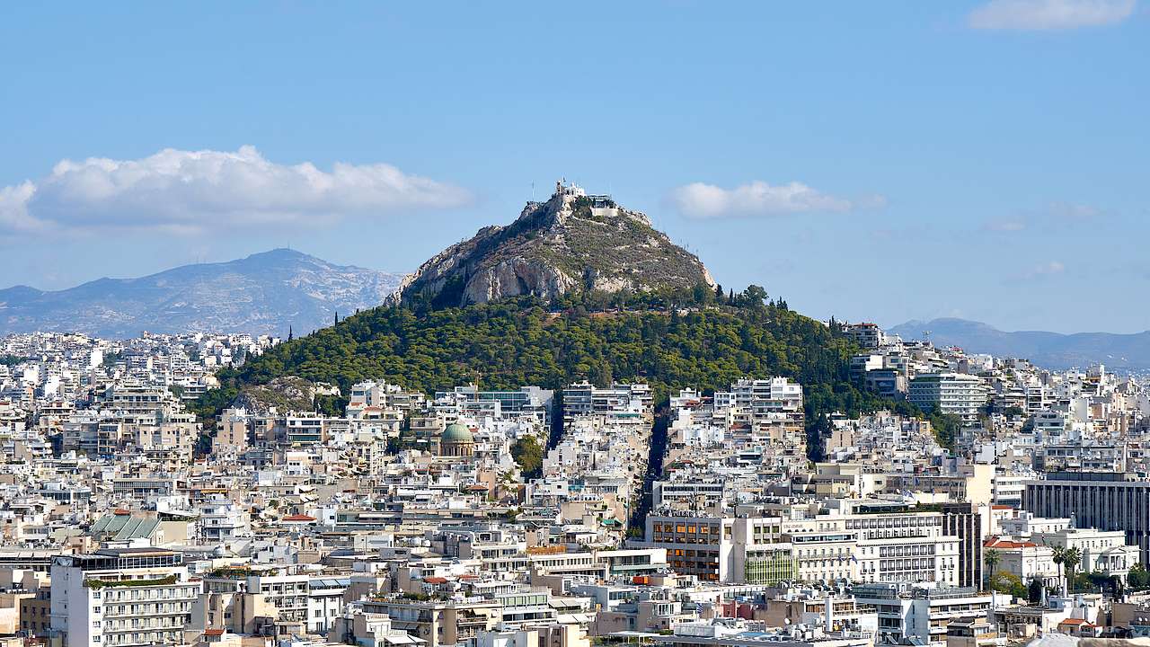 A green mountain at the back with city buildings in front
