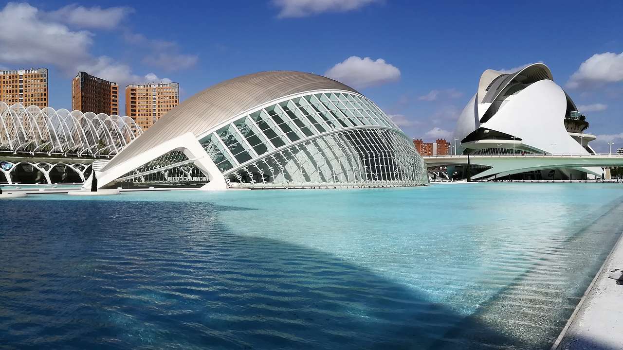 A modern dome-shaped structure next to a pool of water under a blue sky